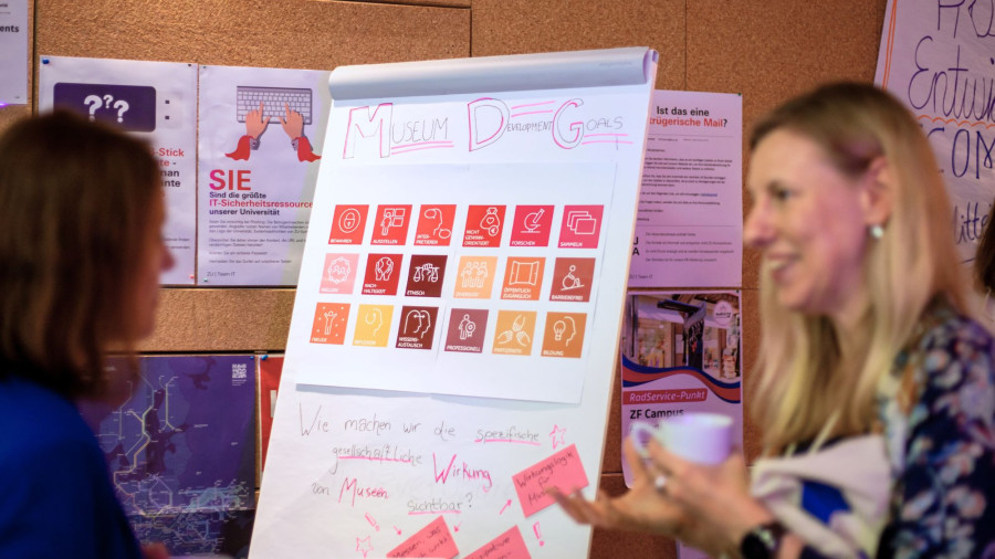 Foto: Nicolas Bühringer. Das Bild zeigt zwei Personen vor einem Flipchart mit der Aufschrift "Museum Development Goals" und bunten Symbolen. Darunter steht handschriftlich die Frage: "Wie machen wir die gesellschaftliche Wirkung von Museen sichtbar?" Es vermittelt eine kreative Workshop-Atmosphäre rund um die Rolle von Museen in der Gesellschaft.